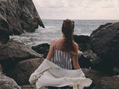 女人在白色细肩带的衣服坐在岩石附近的水域白天
